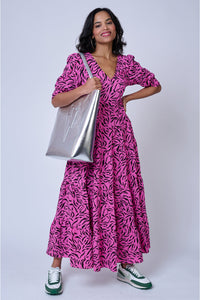 A lady with a silver tote bag wearing a magenta V-neck maxi dress with black zebra and lightning bolt print and trainers