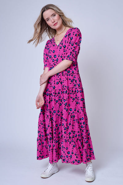 A blonde lady wearing a magenta V-neck maxi dress with blue and black snow leopard & star print, it has short puffed sleeves