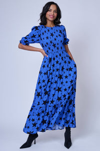 A lady wearing a tiered skirt blue maxi dress with black star and lightning bolt print and black heels