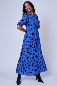A lady wearing a tiered skirt blue maxi dress with black star and lightning bolt print and black heels