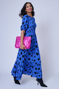 A lady wearing a tiered skirt blue maxi dress with black star and lightning bolt print holding a hot pink swag bag