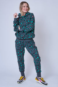 A lady wearing grey with green and black snow leopard and lightning bolt print cosy joggers with a matching hoodie