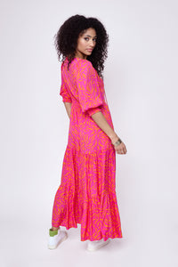 A curly-haired lady looking over her shoulder wearing a pink with orange zebra and lightning bolt print tiered maxi dress