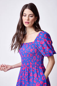 A brown-haired lady wearing an electric blue with hot pink leopard & lightning bolt print shirred midi dress