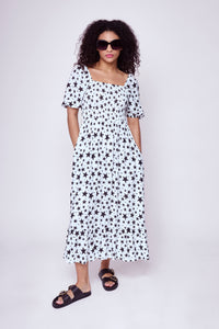 A curly-haired lady wearing a Scamp & Dude shirred midi dress and black oversized sunglasses with gradient smoke lenses