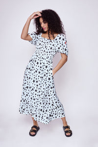 A curly-haired lady wearing an ivory with black star and lightning bolt print shirred midi dress with blouson sleeves