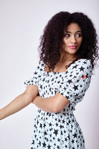 A curly-haired lady wearing an ivory with black star and lightning bolt print shirred midi dress with blouson sleeves