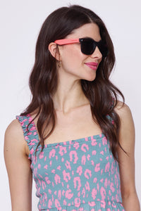 A brunette lady wearing black frame sunglasses with orange and neon pink arms and smoke coloured lenses