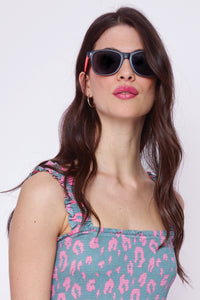 A brunette lady wearing black frame sunglasses with orange and neon pink arms and smoke coloured lenses