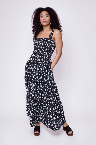 A curly-haired lady wearing a black with white star and lightning bolt print maxi sundress with block heel sandals