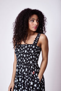 A lady wearing a black with white star & lightning bolt print maxi sundress with a neon pink lightning bolt on the hip