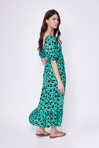 A lady wearing a green with black leopard and lightning bolt print shirred midi dress with blouson sleeves and sandals