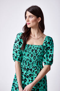 A brunette lady wearing a green with black leopard and lightning bolt print shirred midi dress with blouson sleeves