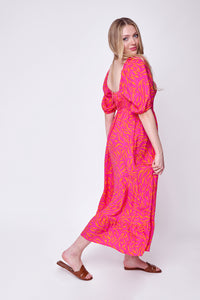 A blonde lady wearing a pink with orange zebra and lightning bolt print shirred midi dress with brown sandals