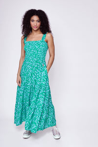 A curly-haired lady wearing a bright green and lilac zebra and lightning bolt print maxi sundress with lilac converse
