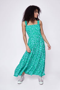 A curly-haired lady wearing a bright green and lilac zebra and lightning bolt print maxi sundress with lilac converse