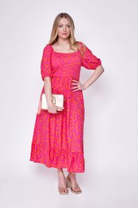 A blonde lady wearing a pink with orange zebra and lightning bolt print shirred midi dress with a rose gold bag and heels