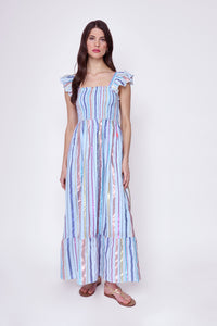 A brunette lady wearing a pale blue with rainbow lurex stripe detail maxi sundress with gold sandals