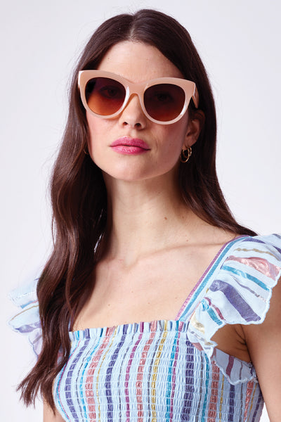 A brunette lady wearing peach cat eye sunglasses with gradient brown lenses with a pale blue with rainbow lurex sundress