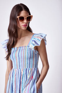 A brunette lady wearing a pale blue with rainbow lurex stripe detail maxi sundress with sunglasses