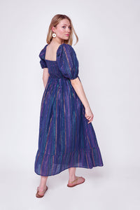 A blonde lady looking over her shoulder wearing a washed navy with rainbow lurex stripe detail shirred midi dress