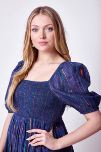 A blonde lady wearing a washed navy with rainbow lurex stripe detail shirred midi dress