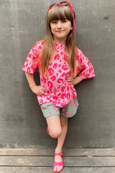 Scamp and Dude | Kids Pink with Neon Pink Leopard T-Shirt | Young girl with hands on hips wearing a pink leopard print top and green lightening bolt shorts with pink sandals