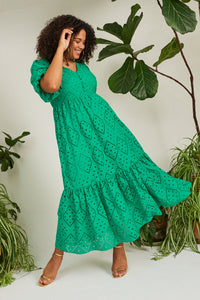 A curly-haired lady wearing a button front green broderie Anglaise midi dress with rose gold heels