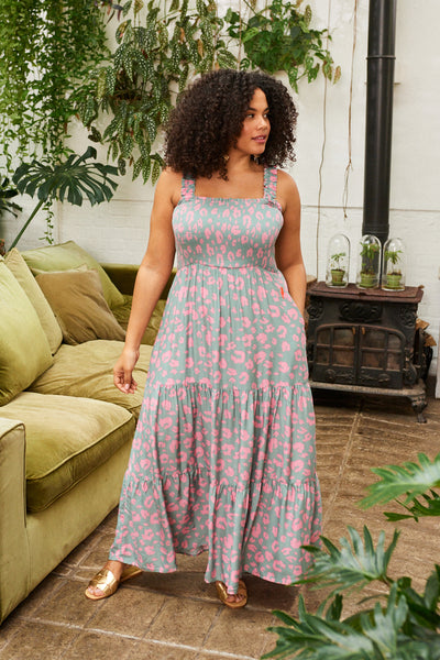 A curly-haired lady wearing a khaki with pink leopard and lightning bolt print tiered maxi sundress with gold sandals