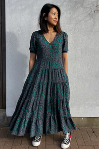 A lady with her hands in her pockets wearing a black and green snow leopard and lightning bolt print v-neck maxi dress
