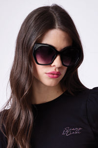 A brunette lady wearing black oversized sunglasses with gradient smoke lenses