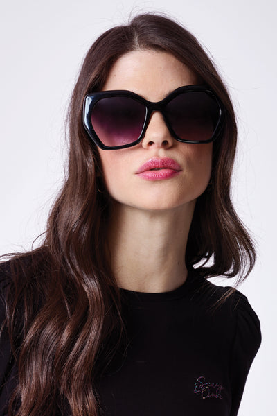 A brunette lady wearing black oversized sunglasses with gradient smoke lenses